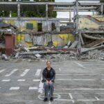 On 16 August 2022 in Kharkiv, Ukraine, Mariia, 12, sits for a portrait in front of the school where she was to enter seventh grade in September. Much of the school was recently destroyed in an air strike, so Mariia will now be studying online when classes resume.