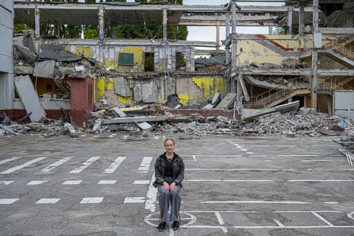 On 16 August 2022 in Kharkiv, Ukraine, Mariia, 12, sits for a portrait in front of the school where she was to enter seventh grade in September. Much of the school was recently destroyed in an air strike, so Mariia will now be studying online when classes resume.