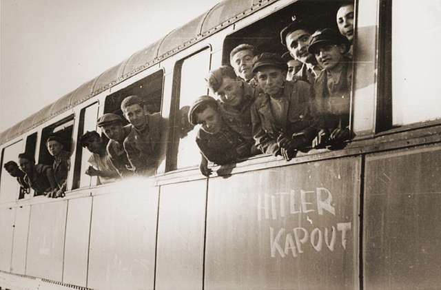 Jewish youth liberated at Buchenwald lean out the windows of a train, as it pulls away from the station. The train, which has been marked with the phrase "Hitler kaput" ("Hitler is finished" in several European languages), will transport the children to an OSE home in Ecouis, France.